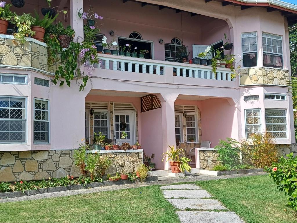 a pink house with a balcony and plants at PeachBloom Terrace Inn in Saint Georgeʼs