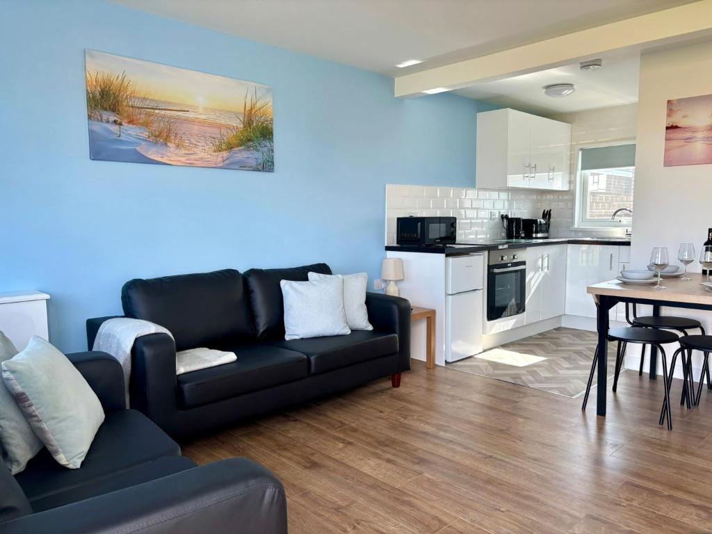 a living room with a black couch and a kitchen at Modern Airy Chalets on popular California Sands Holiday Park - short walk to beach, Nr Norfolk Broads & Great Yarmouth in Scratby