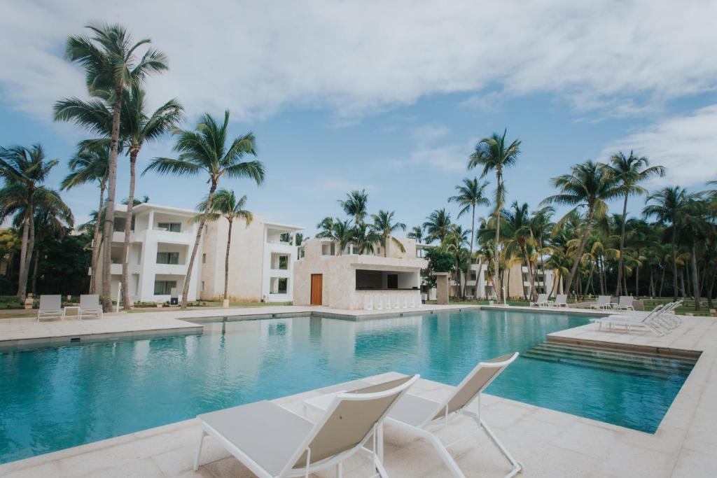 a swimming pool with white chairs and palm trees at Grand Bavaro Princess - All Inclusive in Punta Cana