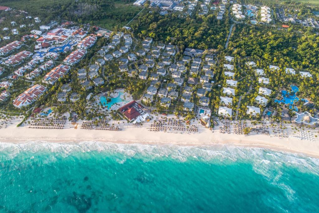 Aerial view of beachfront resort with buildings, pools, beach umbrellas, and turquoise ocean.