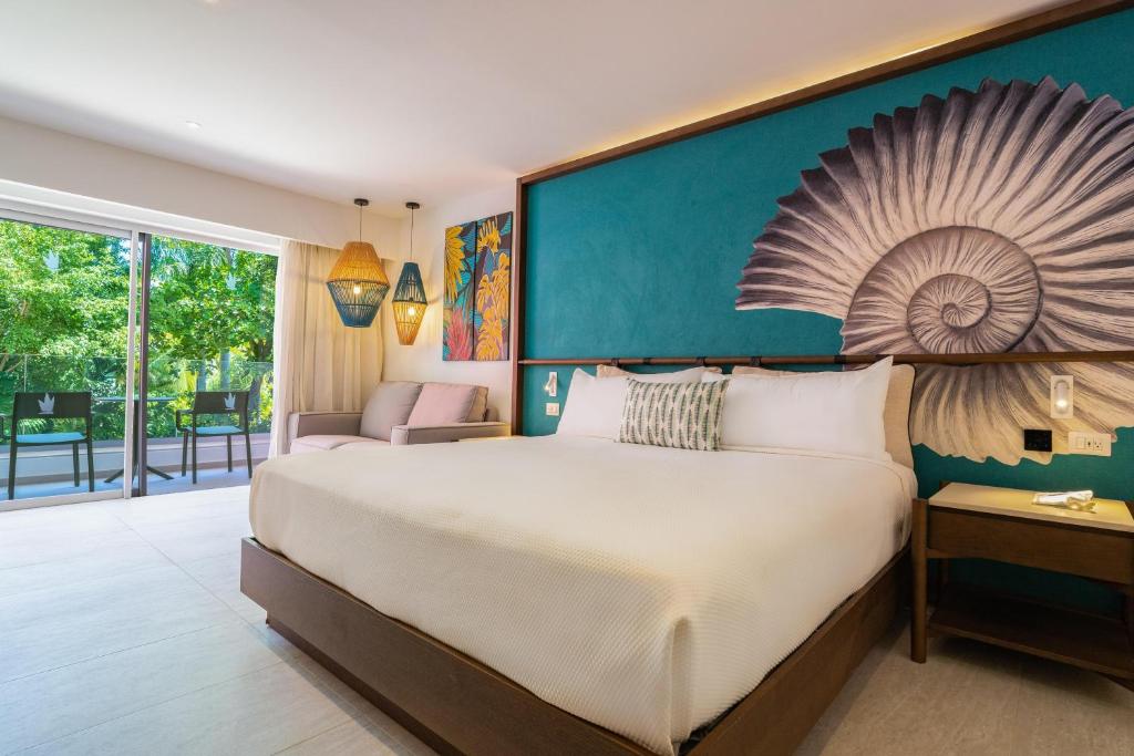 Hotel bedroom with queen bed, teal accent wall, and balcony doors overlooking grounds.