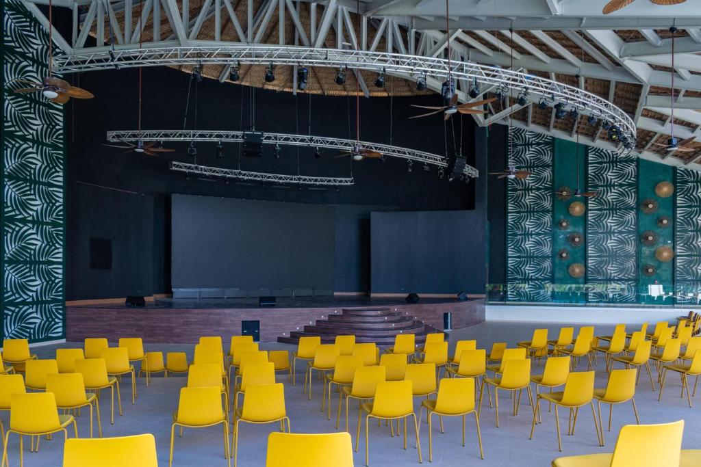 Large stage with yellow chairs arranged for audience seating and professional lighting rigging.