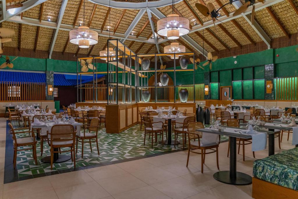 Dining room with round tables, green walls, woven ceiling, and central bar enclosure.