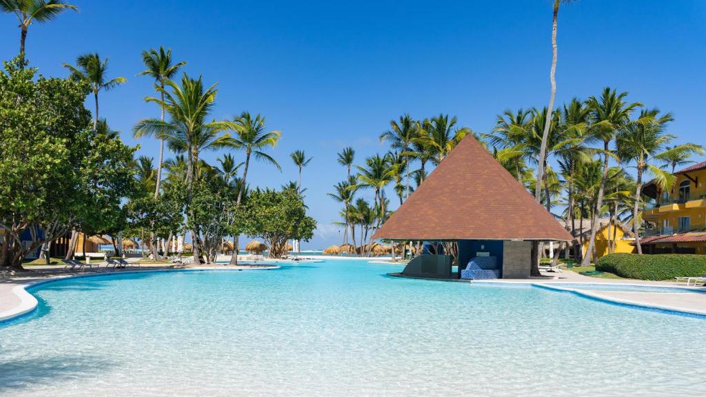 Large shallow pool with thatched roof structure, palm trees, and yellow buildings.