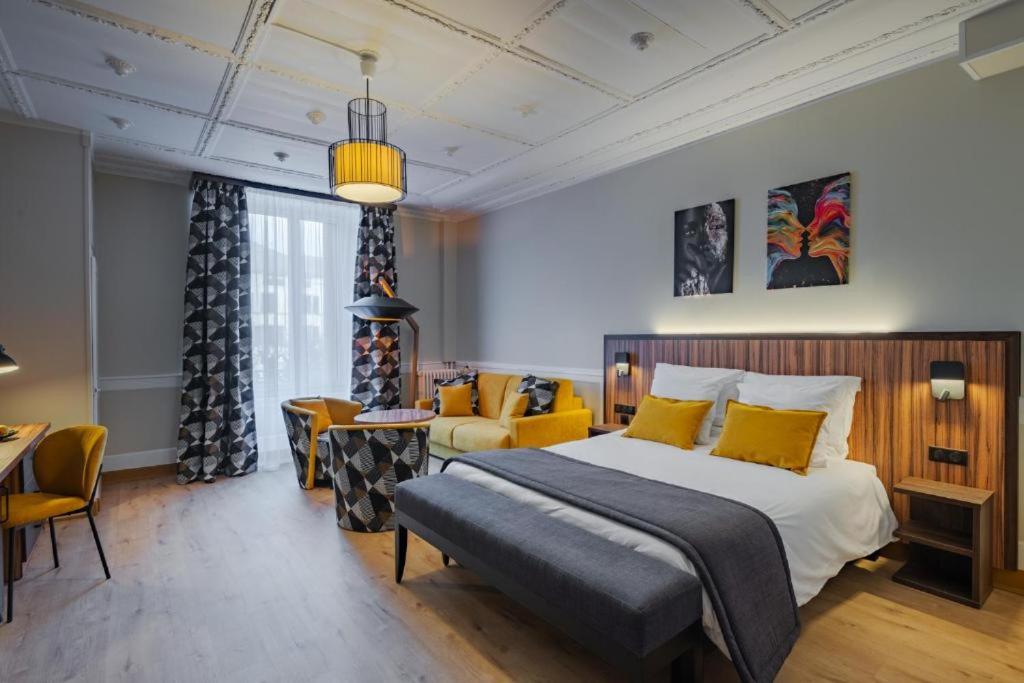 een slaapkamer met een bed en een bank en stoelen bij Hôtel des XII Apôtres & de la Clé des Champs in Contrexéville