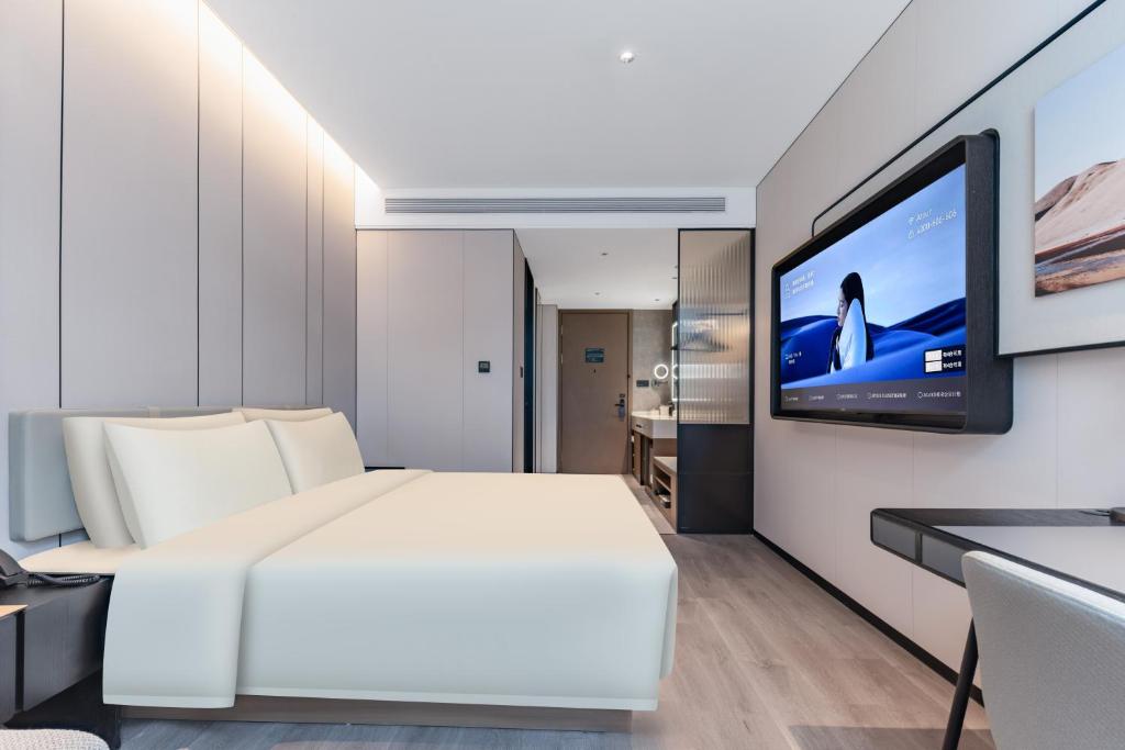 Atour Hotel Shanghai North Bund Dalian Road في شانغهاي: غرفة نوم بسرير ابيض وتلفزيون بشاشة مسطحة