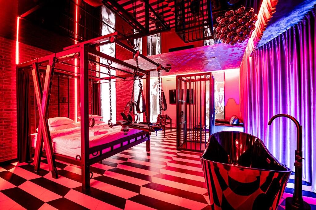 une chambre avec un lit et une baignoire dans une pièce avec des lumières roses dans l'établissement Nikisz Red BDSM, à Katowice