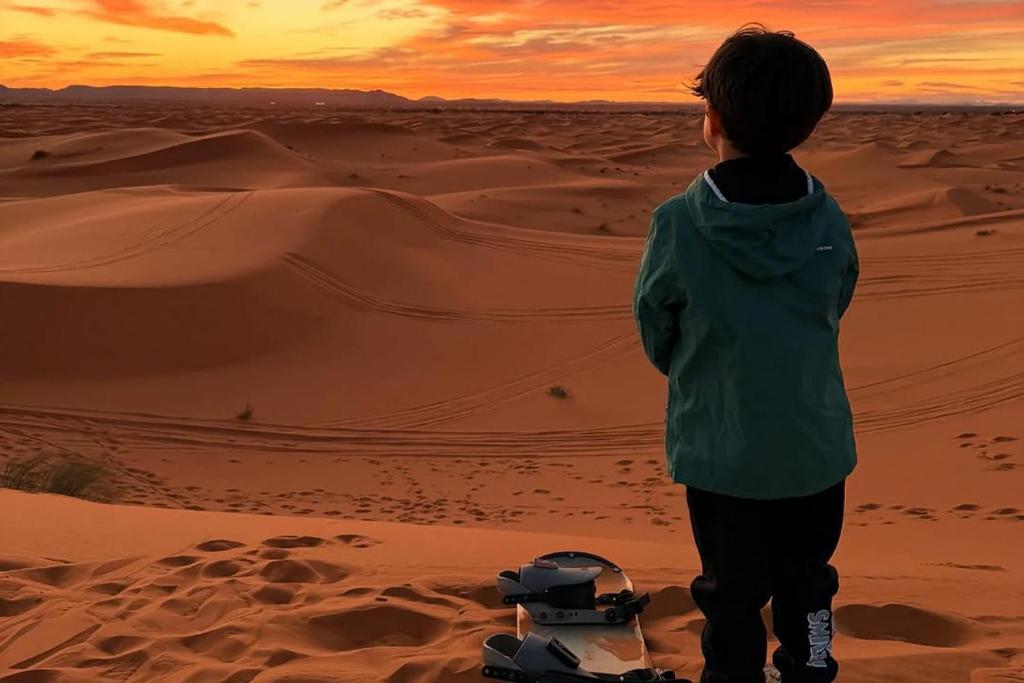 ein kleiner Junge steht bei Sonnenuntergang in der Wüste in der Unterkunft luxury desert night camp in Merzouga
