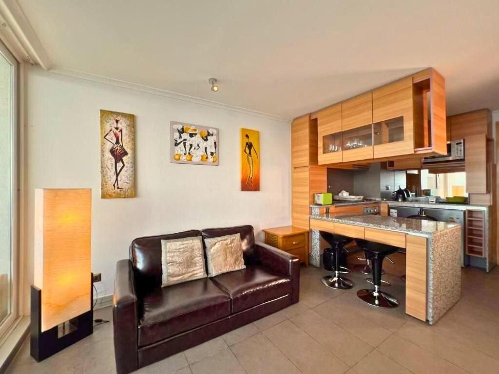 a living room with a leather couch and a kitchen at Hermoso departamento en Costa Horizonte in Concón