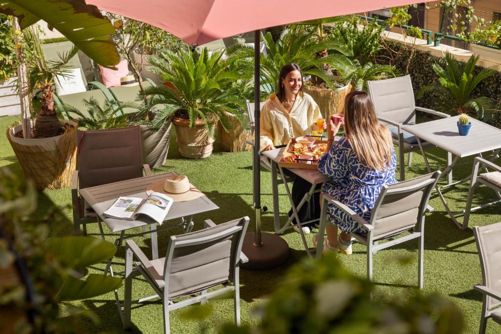 due donne sedute a un tavolo sotto un ombrellone di Hôtel Locarno Nice a Nizza