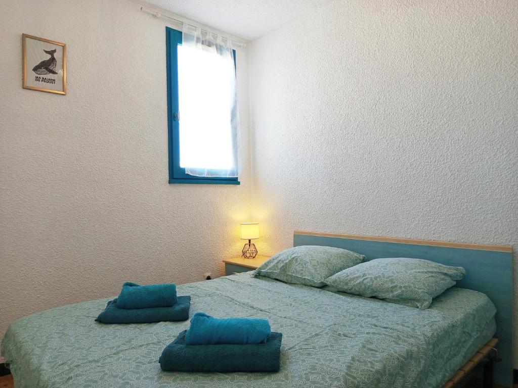 ein Schlafzimmer mit einem Bett mit blauen Kissen und einem Fenster in der Unterkunft La Vie en Rose Cosy Proche du Port in Gruissan