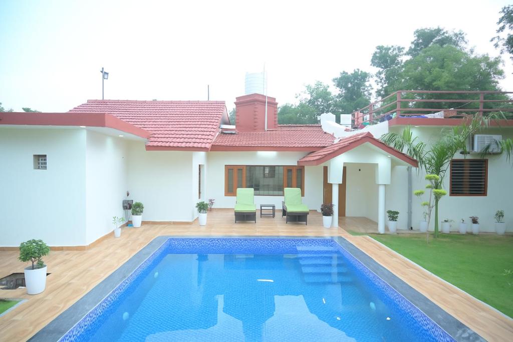 a villa with a swimming pool in front of a house at Aravali Farm Gurgaon, 3 Bedroom Villa with Lawn Barbeque Grill and Pool in Gurgaon