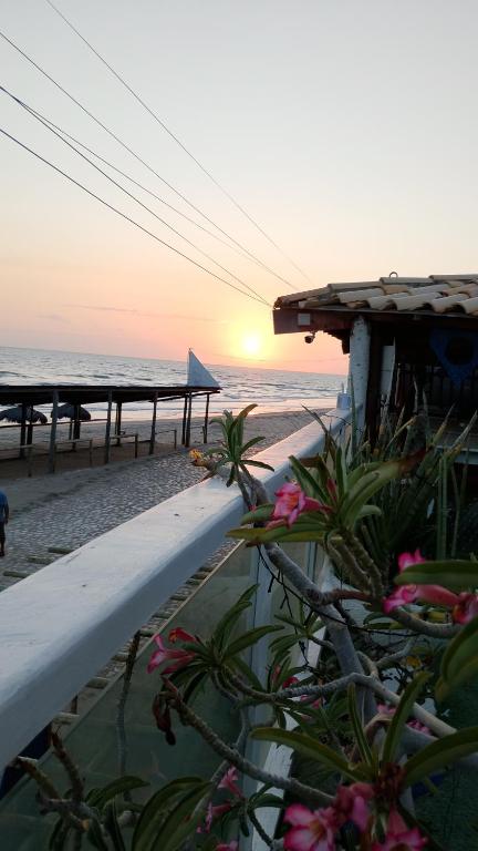 a sunset over the beach with a house and flowers at Beiral Pousada E Restaurante in Ponta do Mel