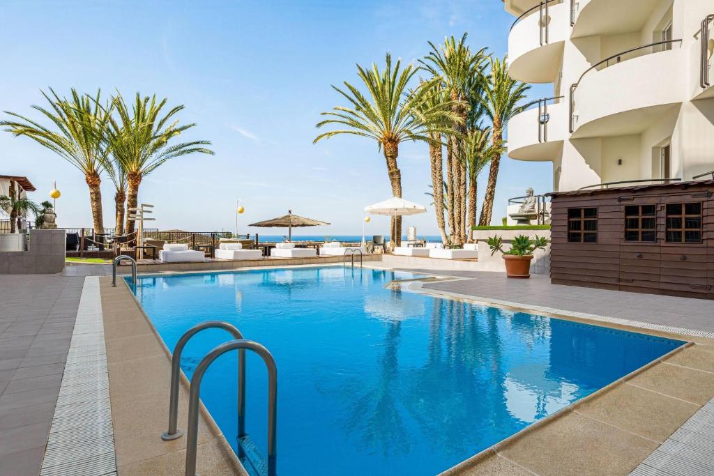 a swimming pool with palm trees and a building at Ramada Resort by Wyndham Puerto de Mazarron in Puerto de Mazarrón