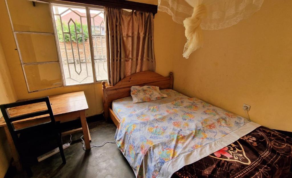 a bedroom with a bed and a desk and a window at Bonnie's Homestay in Gasanze