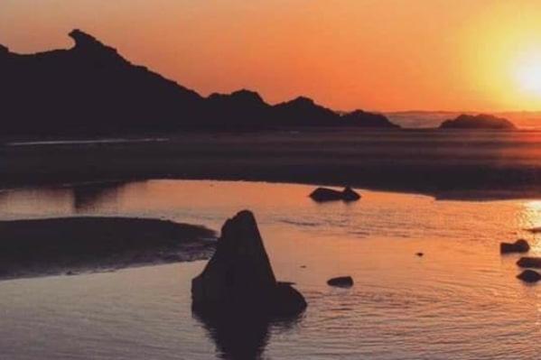 a large rock in the water at sunset at By the Beach Perranporth, Truro, cornwall in Perranporth