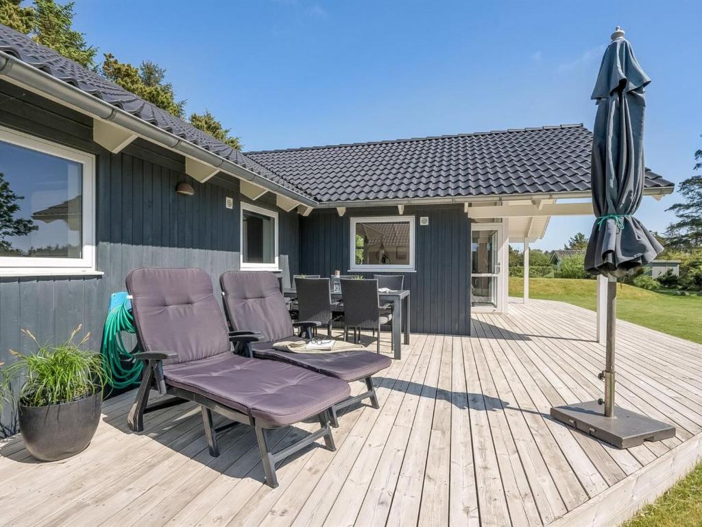 une terrasse en bois avec deux chaises et un parasol dans l'établissement Holiday Home Elina - 600m from the sea by Interhome, à Blåvand