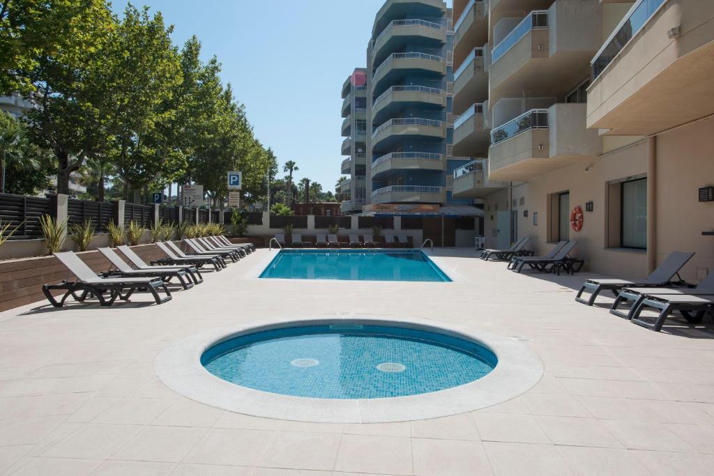 una piscina en medio de un patio con sillas y un edificio en Apartamentos California en Salou
