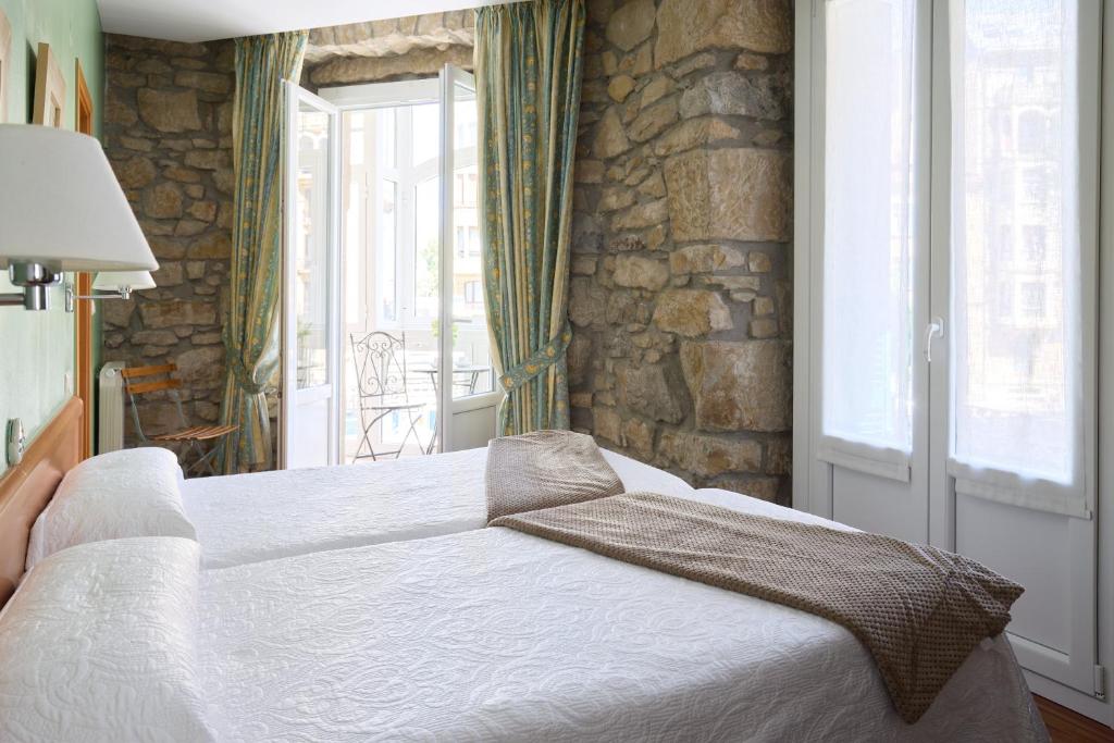 a bedroom with a white bed and a stone wall at Pensión Nuevas Artes in Donostia-San Sebastián