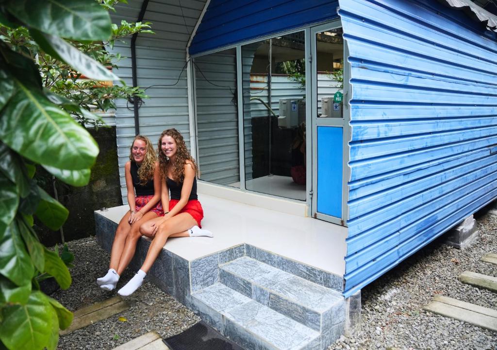 Dos mujeres sentadas en el porche delantero de una pequeña casa. en A4 Hostel Colombo Airport Lounge - By A4 Transit Hub-Free Shuttle Pick Up & Drop 24HRS, en Katunayake