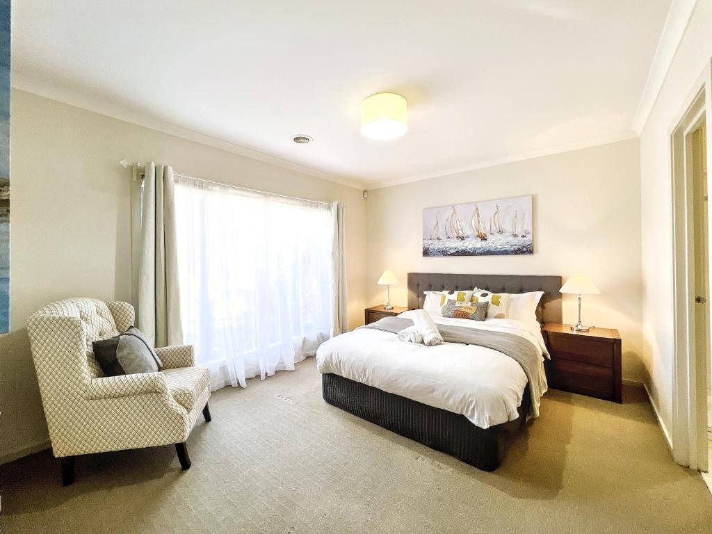 Un dormitorio con una cama y una silla y una ventana. en Modern Golfside Retreat, en Carrum Downs