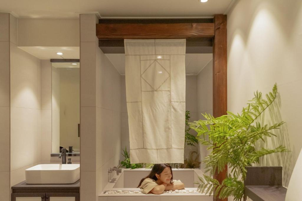 a young girl sitting in a bathroom in front of a mirror at Maisonde Onu Jeonju in Jeonju