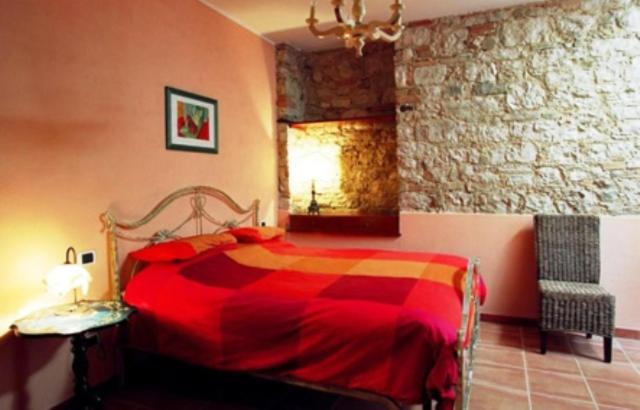 1 dormitorio con cama roja y pared de piedra en Perbacco en SantʼAngelo Limosano