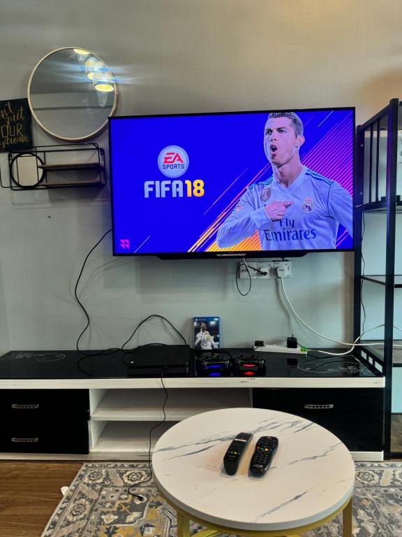 a flat screen tv on a wall with two remote controls at AYAAN Flora Quintet Apartment & Fifa Home 4 with Free Parking in Tanah Rata