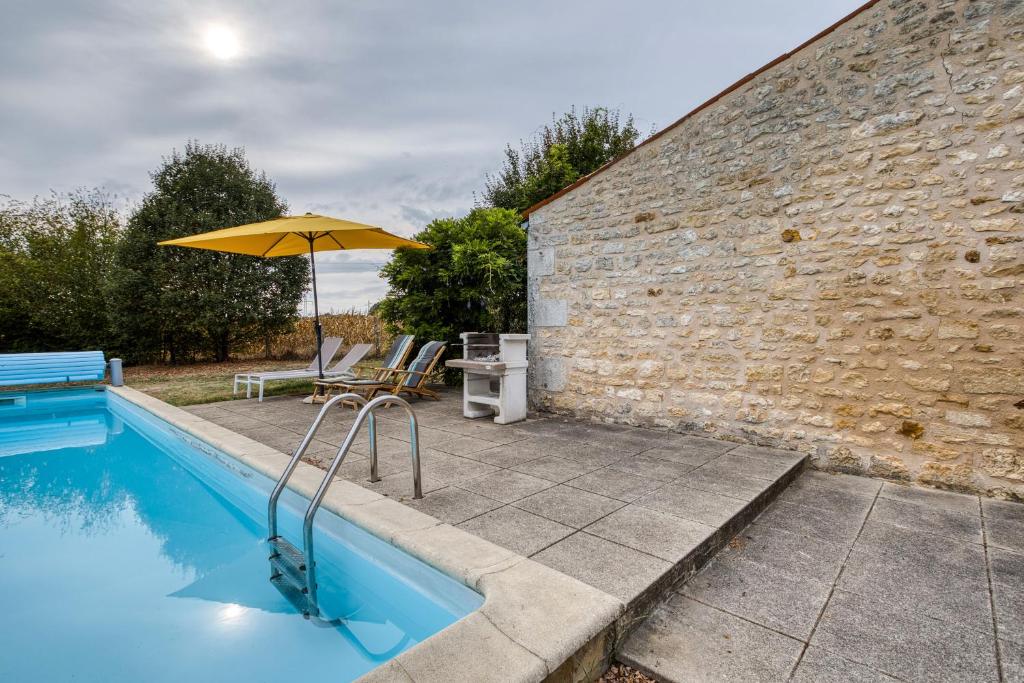 a pool with an umbrella next to a brick wall at La musardière in Saint-Germain-du-Seudre
