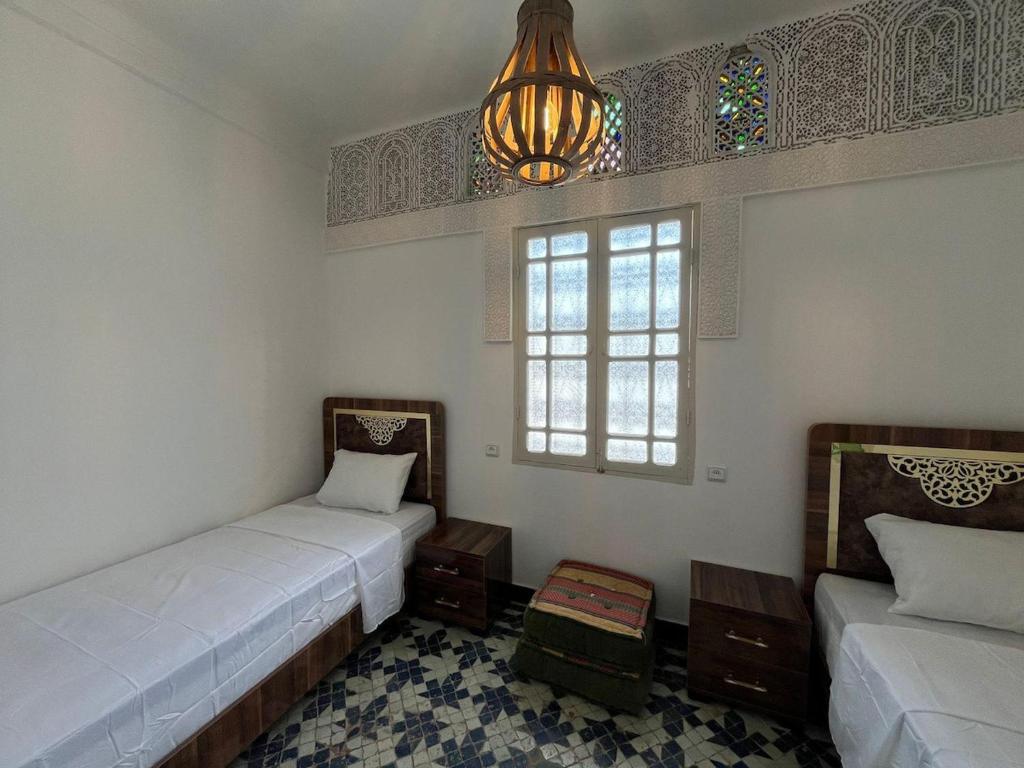 a room with two beds and a window and a chandelier at Dar Latifa in Fès