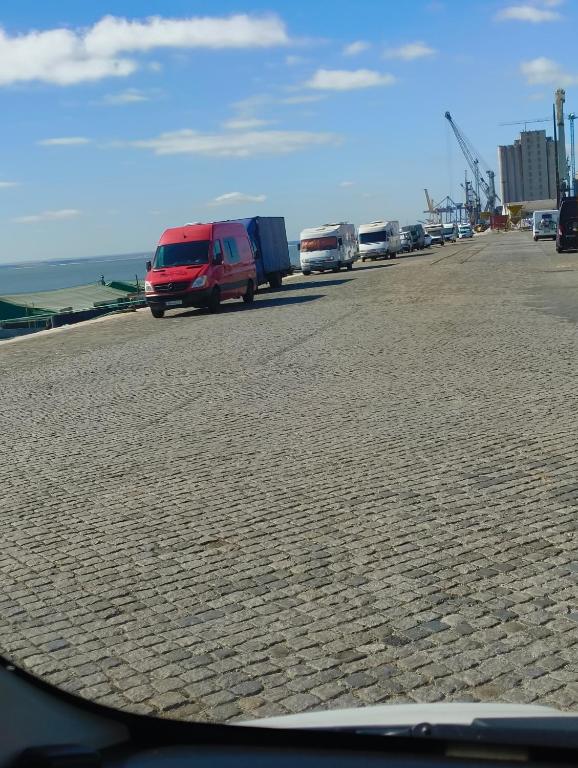 a group of cars parked on a road with the ocean at Caravana Poço Bispo in Lisbon
