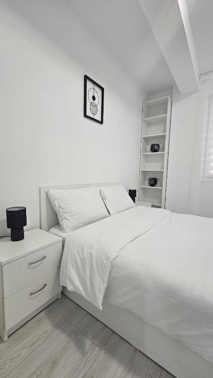 a white bedroom with a white bed and a shelf at Apartament Alb&Negru in Sebeş