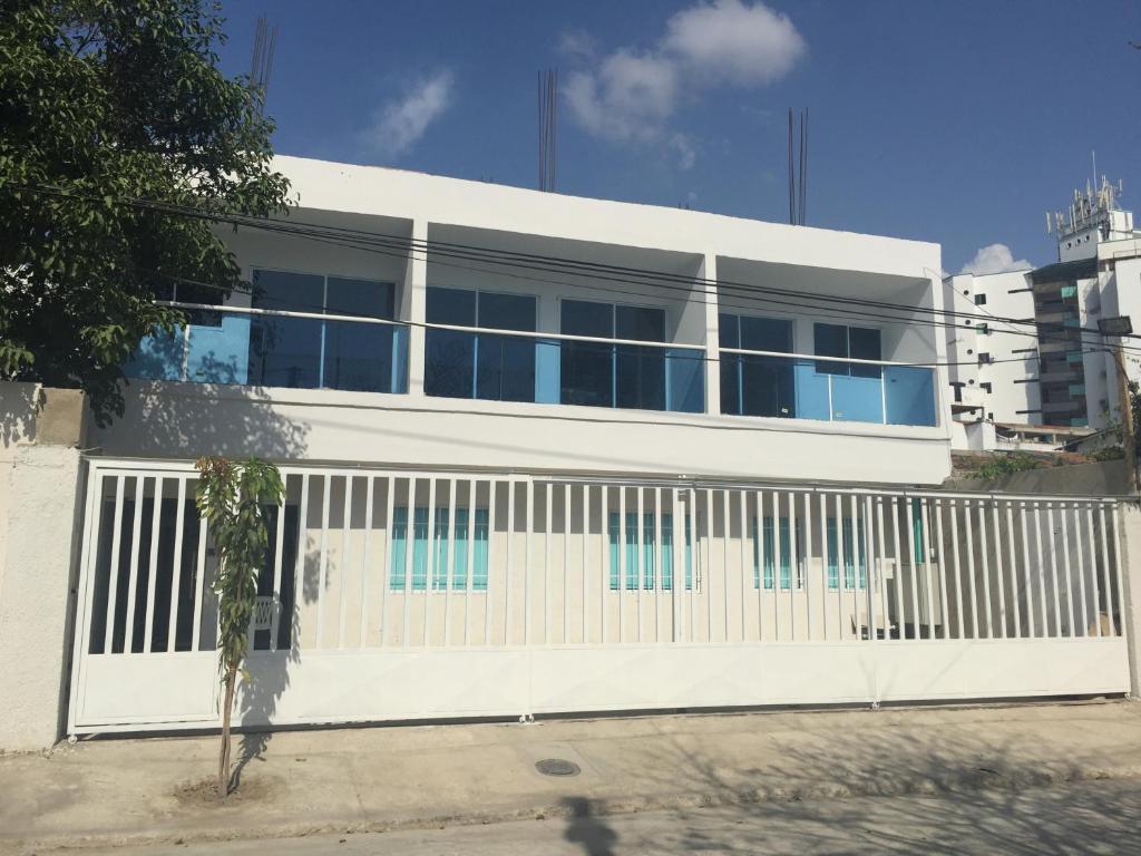 a white building with blue windows and a fence at Mayva AprtaHotel in Santa Marta