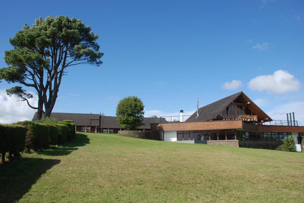 a house on a hill with a tree in the foreground at Panamericana Hotel Ancud in Ancud