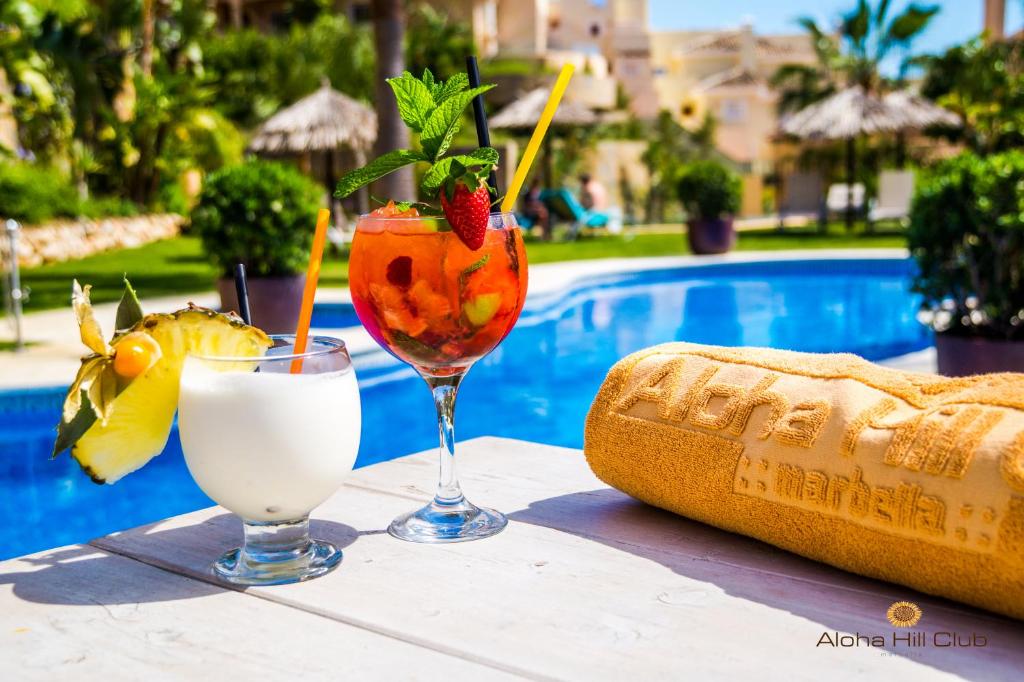 zwei Getränke auf einem Tisch neben einem Pool in der Unterkunft Aloha Hill Club in Marbella