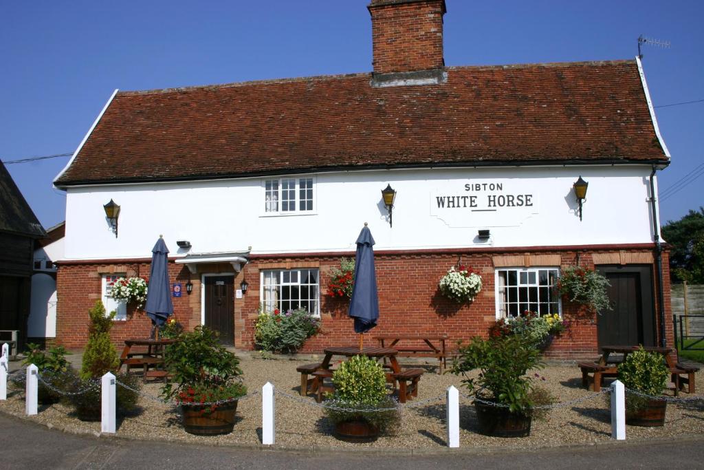 uma casa branca com bancos e guarda-chuvas à sua frente em Sibton White Horse Inn em Saxmundham