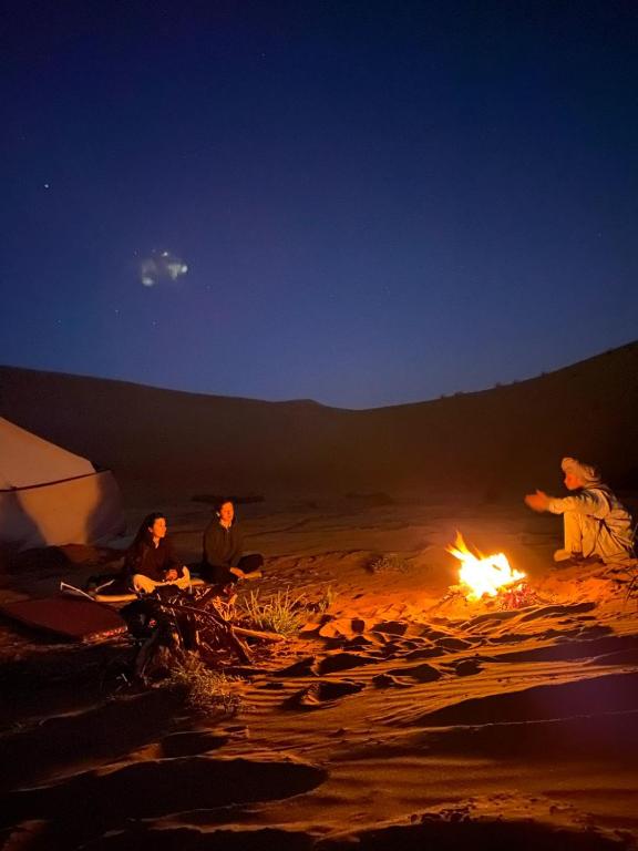 a group of people sitting around a fire in the desert at The dune camp in Mhamid