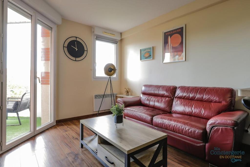 ein Wohnzimmer mit einem roten Ledersofa und einem Tisch in der Unterkunft Montaigne - Proche Tram - 5min Aéroport in Blagnac