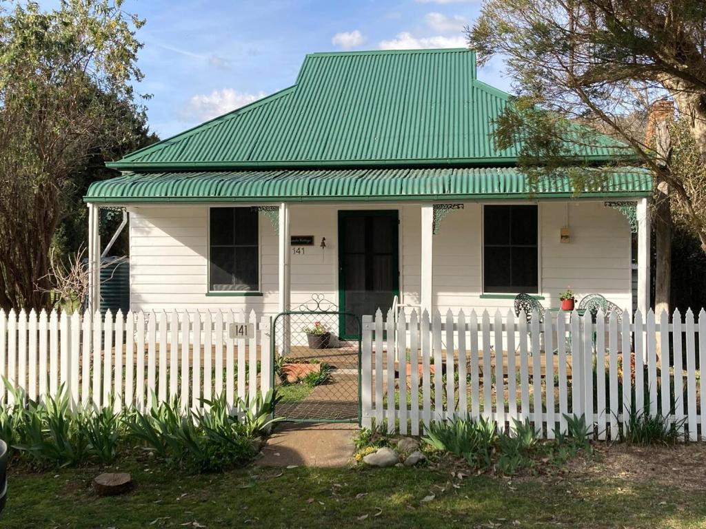 a white house with a green roof behind a white picket fence at Lavender Cottage in Sofala