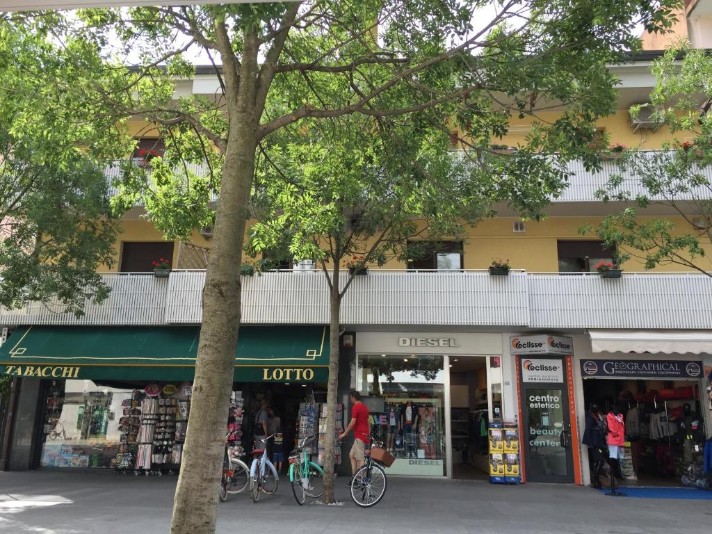 un groupe de magasins dans une rue arborée dans l'établissement Condominio Belletti, à Lignano Sabbiadoro
