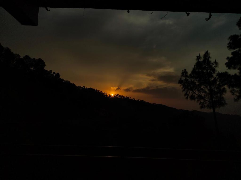 a sunset over a hill with a tree in the foreground at The Moonlight Stay Kasauli in Kasauli