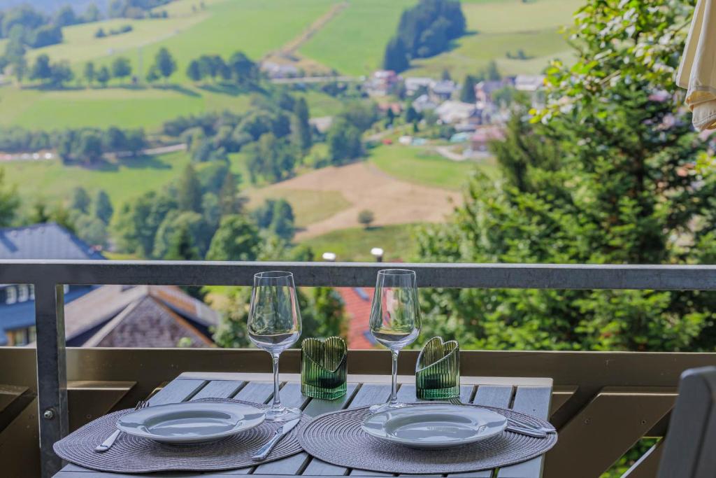 a table with two wine glasses and plates on a balcony at Direkt an Wanderwegen Balkon mit traumhafter Aussicht Sauna im Haus Tiefgarage E-Ladestation in Todtnauberg