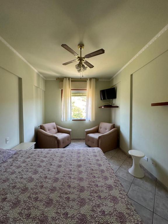ein Schlafzimmer mit einem Bett und zwei Stühlen und einem Fenster in der Unterkunft Apartamento Hotel Cavalinho Branco in Águas de Lindóia