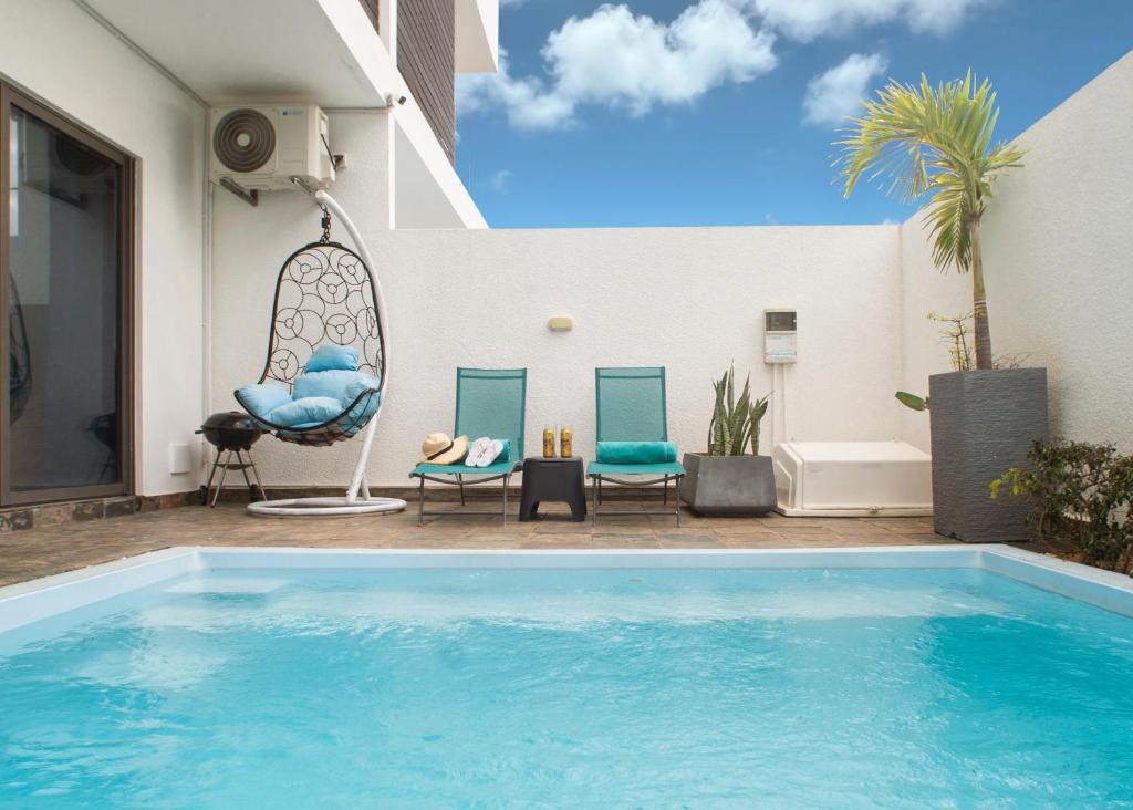 - une piscine à côté de deux chaises et d'une maison dans l'établissement Ocean Blue Villa, Flic-en-Flac, à Flic-en-Flac