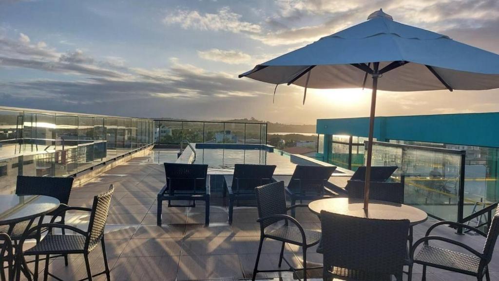 een terras met tafels, stoelen en een parasol bij Flat Varandas do Porto Residence in Porto De Galinhas