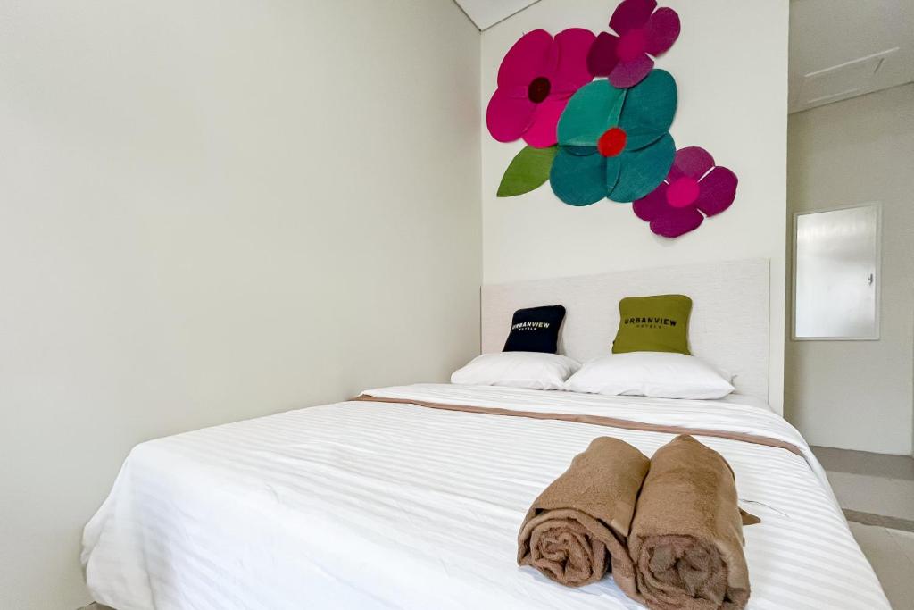 万隆Urbanview at Ra Residence Buah Batu的卧室配有一张铺有白色床单的床,墙上挂着鲜花。