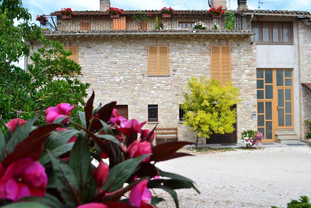 Um velho edifício de pedra com flores cor-de-rosa à frente. em Camere I Monelli em Assis