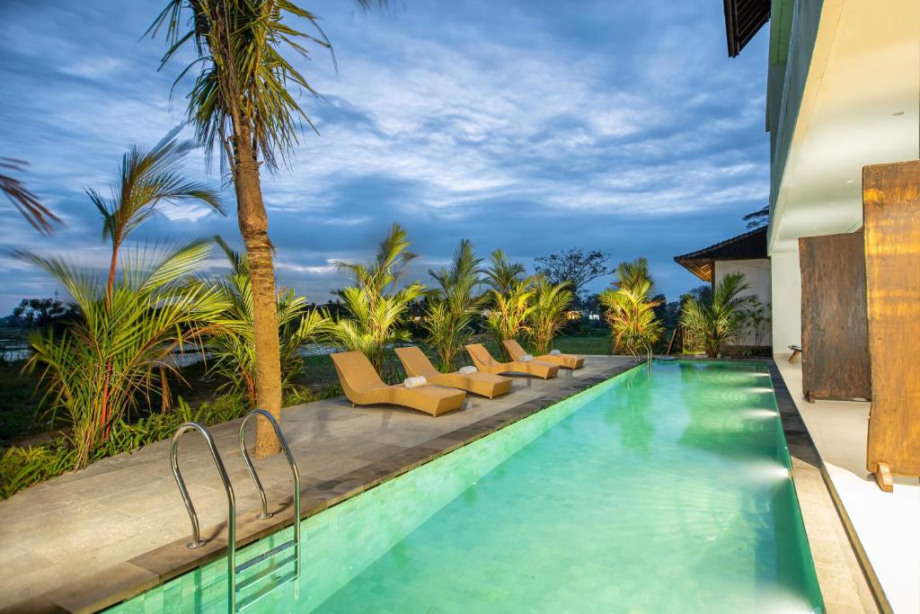 a swimming pool with lounge chairs and palm trees at Kayun Retreat Mas Suite in Ubud