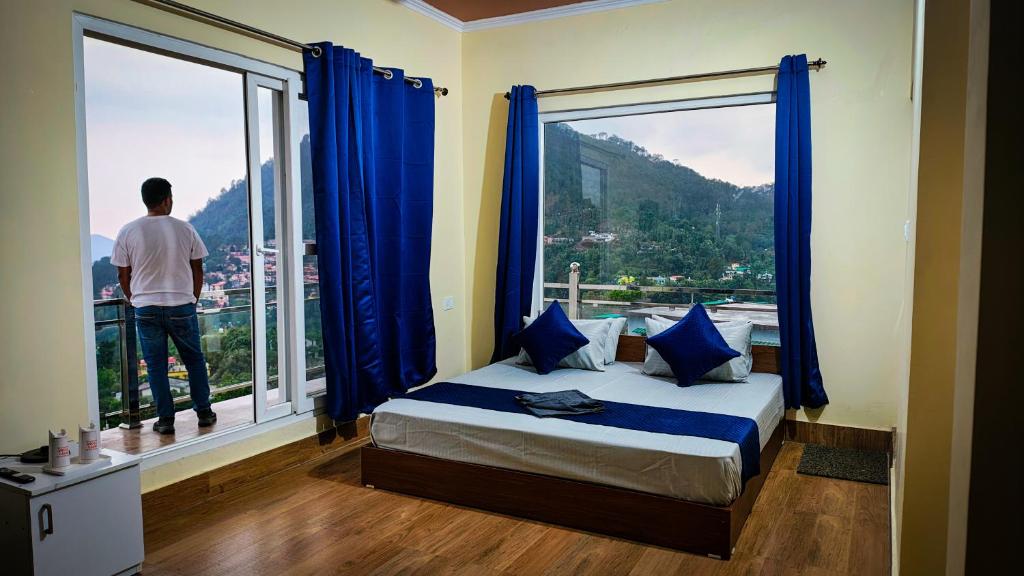 a man looking out the window of a bedroom at Host Labs Homestay - Premium View in Bhīm Tāl
