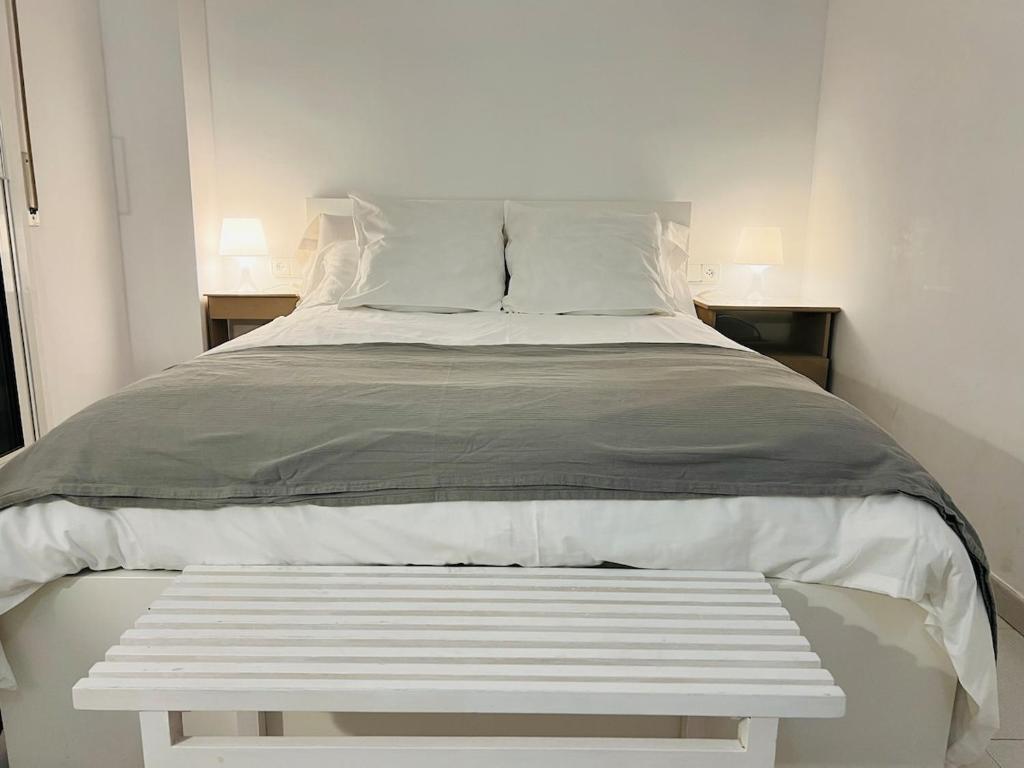Una cama blanca con un banco blanco en una habitación. en Acojedor apartmento, centro con patio, en Sabadell